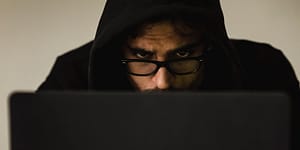 crop focused hacker in hood using laptop
